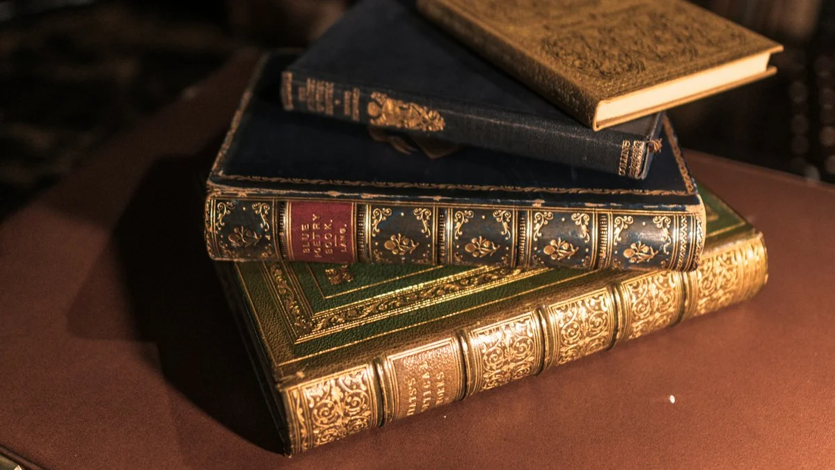 A stack of worn ornate hardbound books in green, gold, and blue rests on a dark leather table. — a The Obsidian Key guide to The Burnout Book That Treats Exhaustion as Signal.