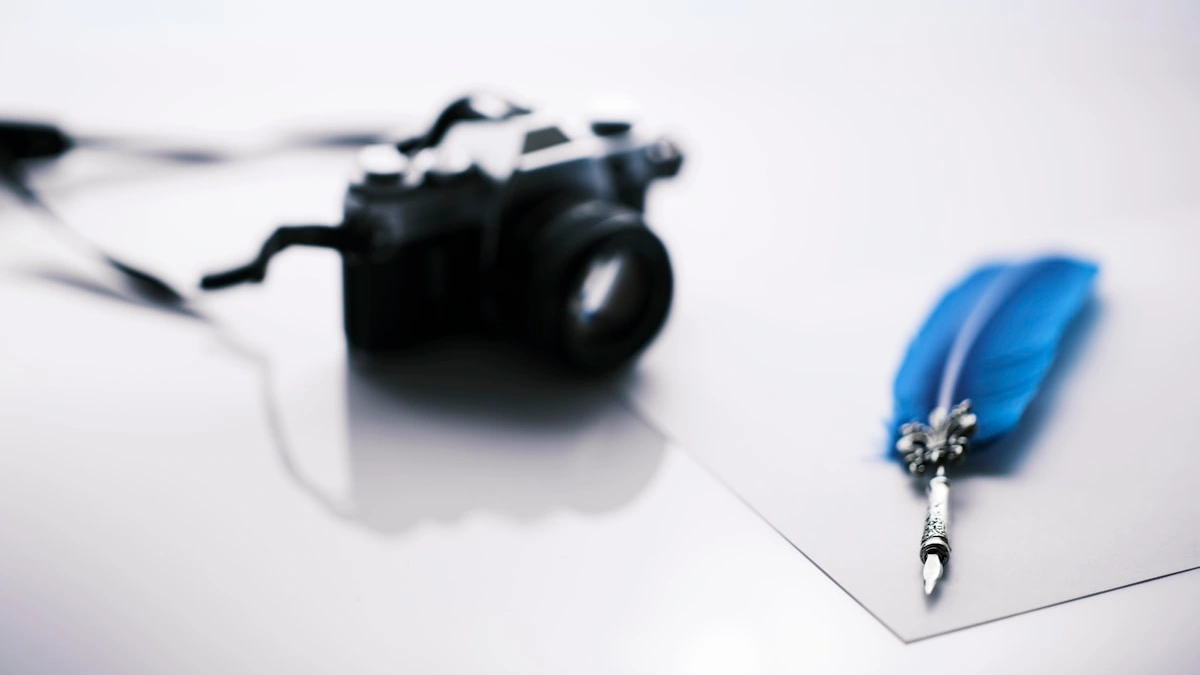 A blue feather quill pen rests on a sheet of paper beside a vintage camera in soft light. — a The Obsidian Key guide to Get the Daily Ritual Template: Start Tomorrow at Dawn.