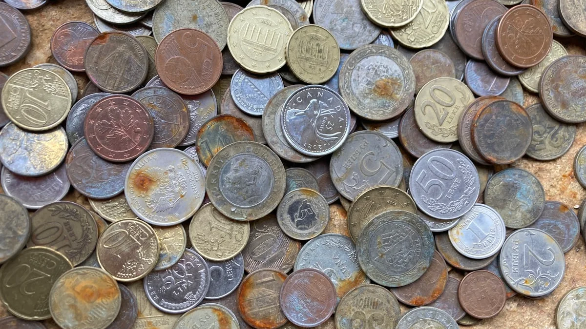 A dense pile of tarnished copper and silver coins covers the frame. — a The Obsidian Key guide to Seven Money Mindset Mistakes the Book Names.