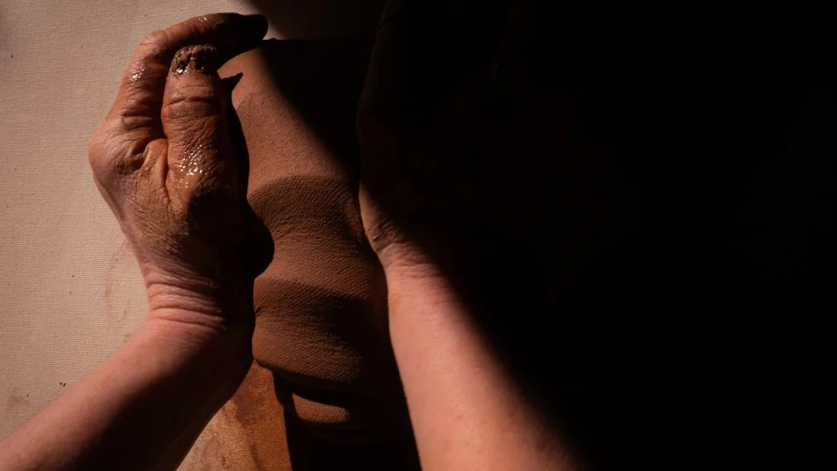 Two weathered hands rest on soft clay in a shaft of warm low light. — a The Obsidian Key guide to The Nine Breaths: A Step-by-Step Breathing Technique.