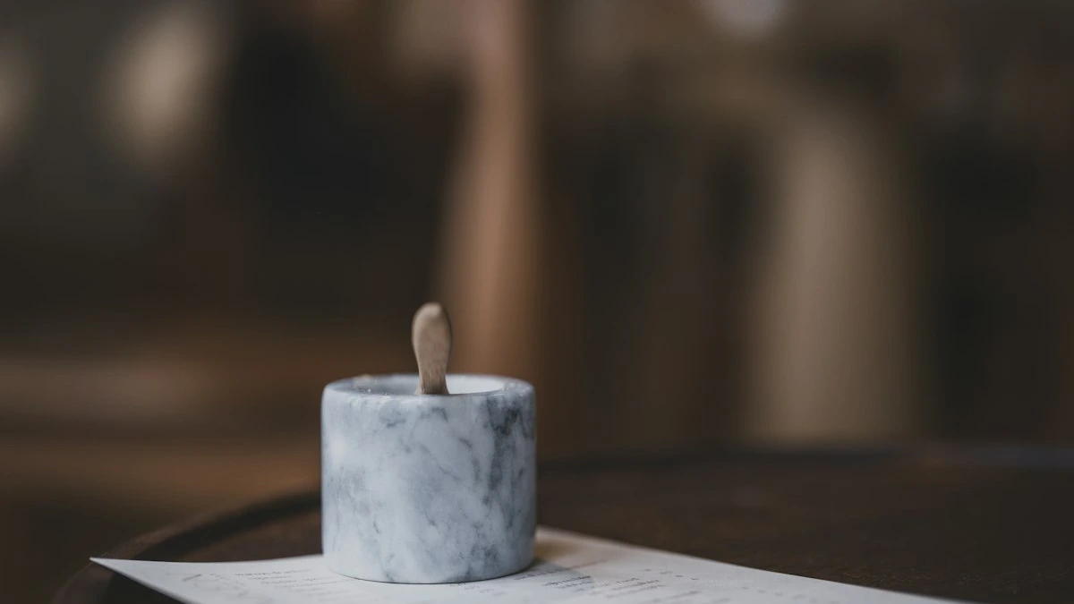 A marble salt cellar with a small wooden spoon rests on a paper menu on a dark round table. — a The Obsidian Key guide to Salt Sound Smoke: Tools That Hold Focus.