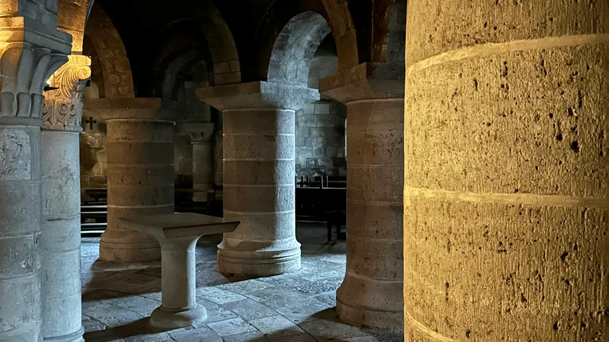 Massive stone pillars and rounded arches in a warm-lit crypt beneath a church. — a The Obsidian Key guide to The Architecture: The Hidden Layer Defined.